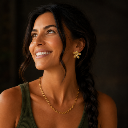 Lächelndes Model trägt goldene Blütenohrringe und eine goldene Kette.