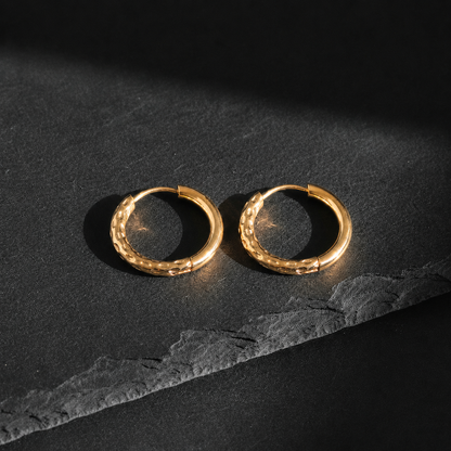 Goldene gehämmerte Creolen auf dunklem Schieferuntergrund mit warmem Licht