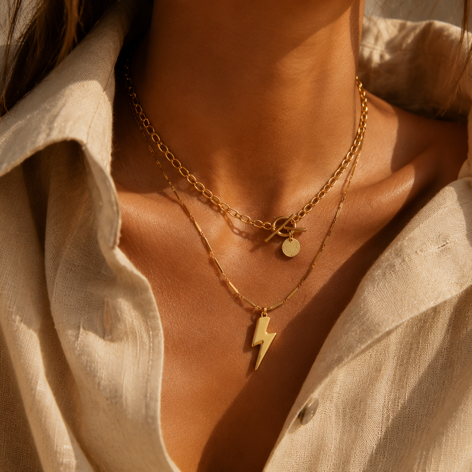 Goldfarbene Edelstahlketten im Layering-Look an einem Model mit heller Bluse in warmem Sonnenlicht.