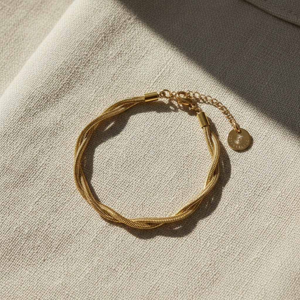 Intreccia Armband in Gold auf beigem Leinenstoff.
