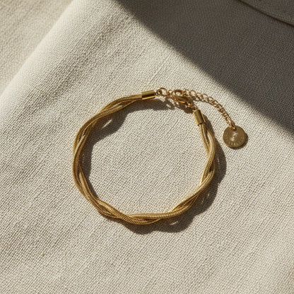 Intreccia Armband in Gold auf beigem Leinenstoff.