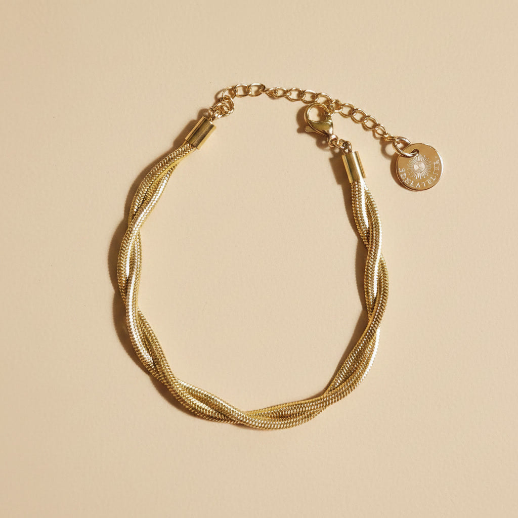 Goldfarbenes Intreccia Armband mit gedrehter Struktur auf beigem Hintergrund.