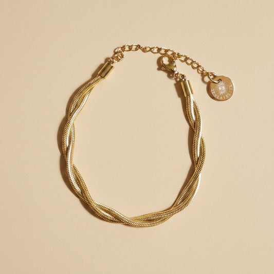 Goldfarbenes Intreccia Armband mit gedrehter Struktur auf beigem Hintergrund.