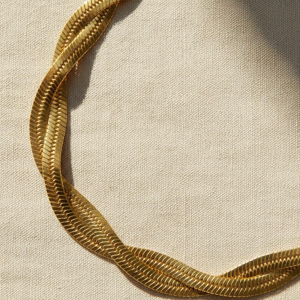 14 Karat vergoldetes geflochtenes Edelstahlarmband auf naturfarbenem Leinenstoff im warmen Licht.