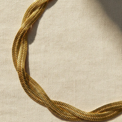 14 Karat vergoldetes geflochtenes Edelstahlarmband auf naturfarbenem Leinenstoff im warmen Licht.