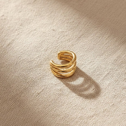 Goldener Intreccio Ear Cuff auf beigem Leinenstoff.