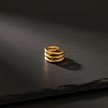 Dreireihiger Intreccio Ear Cuff aus vergoldetem Edelstahl auf dunklem Untergrund.