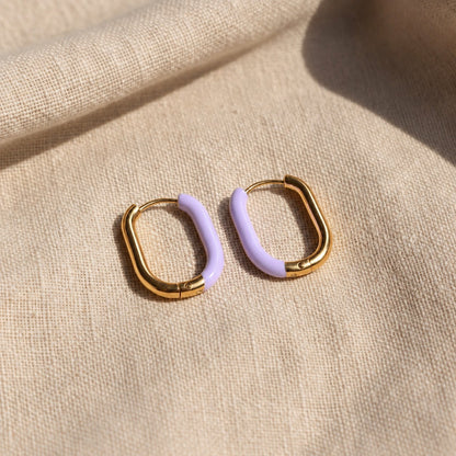 Lavanda Creolen Gold Lavendel auf beigem Leinen, ovale Form und lavendelfarbener Kunstharz-Akzent sichtbar.