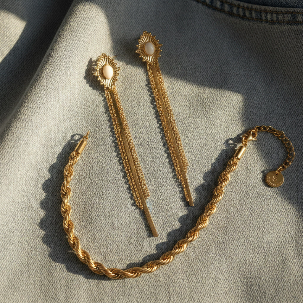 Goldfarbene Luce Fransenohrringe mit Cabochon und passenden Schmuckstücken auf hellem Stoff.