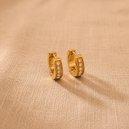Goldene Lucia Creolen mit Zirkonia auf hellem Leinenstoff.