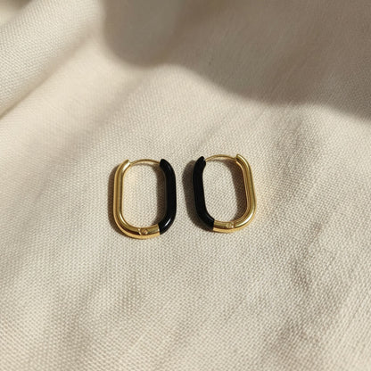 Nera Creolen in Gold und Schwarz frontal auf beigem Leinen, ovale Form und schwarzer Resin-Akzent sichtbar.