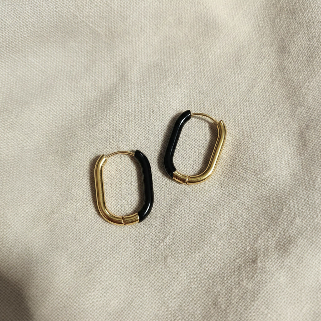 Nera Creolen Gold Schwarz in schräger Produktansicht auf beigem Leinen.