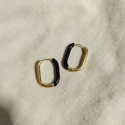 Nera Creolen Gold Schwarz in schräger Produktansicht auf beigem Leinen.