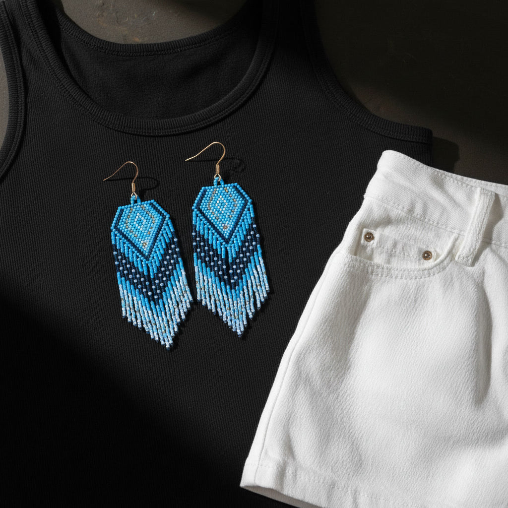 Ein modisches Flatlay-Arrangement zeigt die blau-türkisen Statement-Ohrringe auf einem schwarzen Oberteil, kombiniert mit einer weißen Hose. Die kräftigen Farben der Ohrringe bilden einen lebendigen Kontrast zum schlichten, eleganten Outfit.