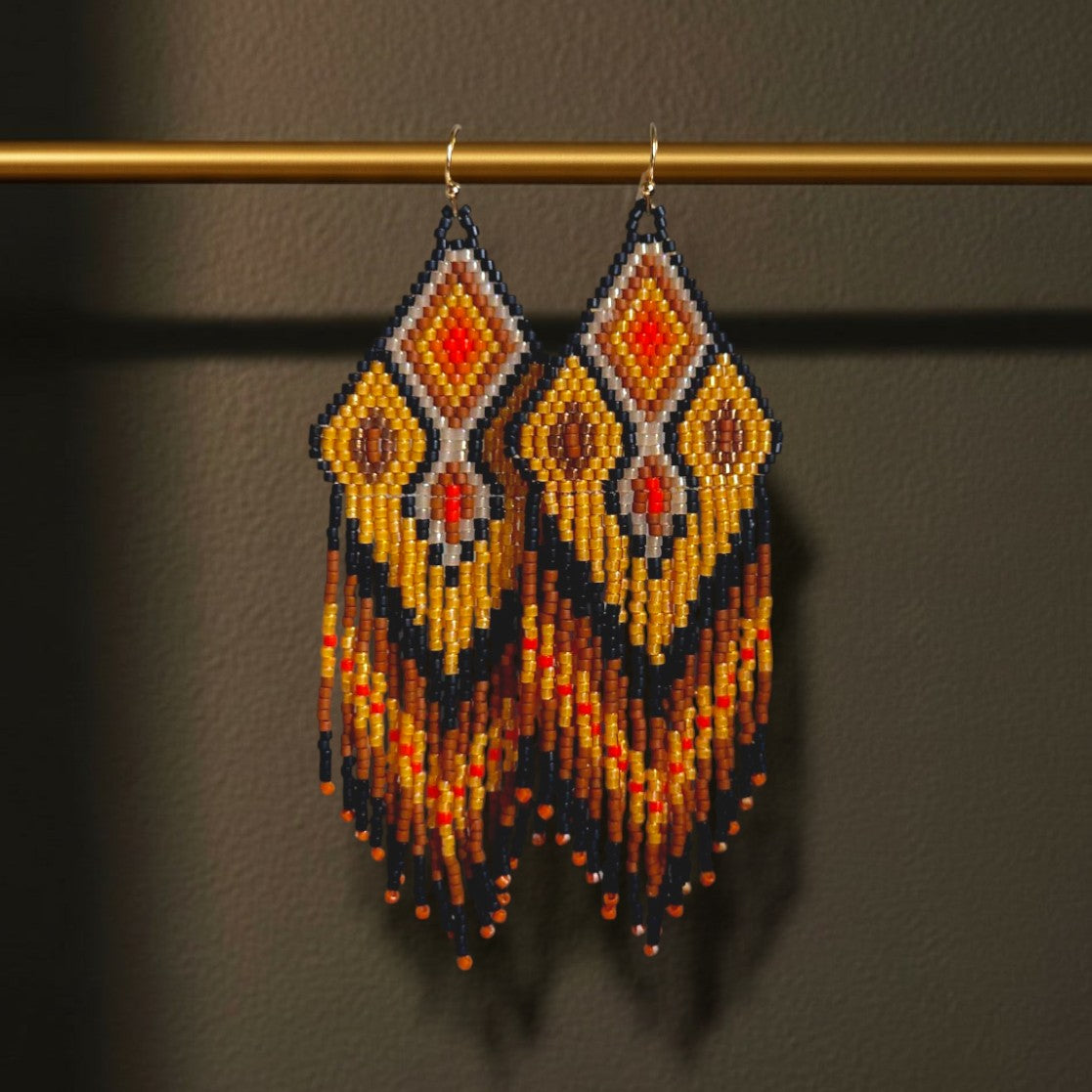 Handgewebte Perlenohrringe Ocra Nera von EDELATELIER. mit Rautenmuster in Schwarz, Ocker und leuchtendem Orange an einem goldfarbenen Stab präsentiert.