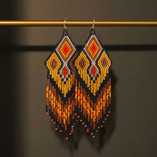 Handgewebte Perlenohrringe Ocra Nera von EDELATELIER. mit Rautenmuster in Schwarz, Ocker und leuchtendem Orange an einem goldfarbenen Stab präsentiert.