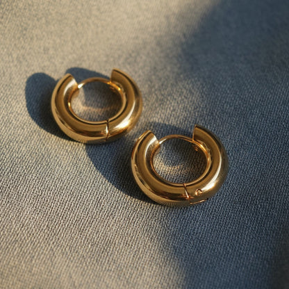 Orbita Creolen aus vergoldetem Edelstahl auf Denimstoff mit warmem Licht und Schatten.
