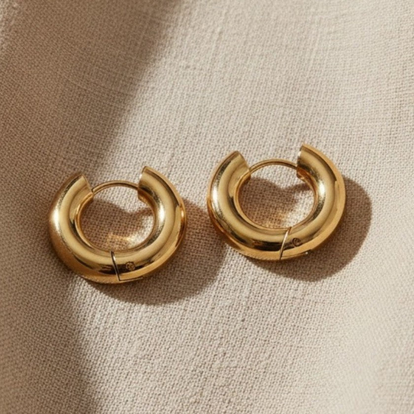 Orbita Creolen in Gold auf hellem Leinenstoff mit warmem Licht und Schatten.