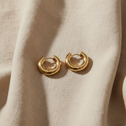 Goldfarbene Orbita Creolen auf hellem Leinenstoff im natürlichen Sonnenlicht.