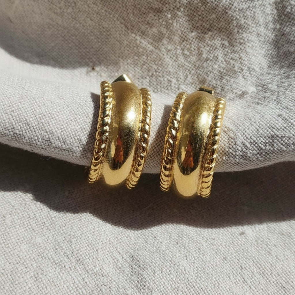 Ornella Chunky Creolen Gold aus Edelstahl 304L mit 18K PVD-Vergoldung und dekorativer Kordelstruktur auf hellem Stoff.