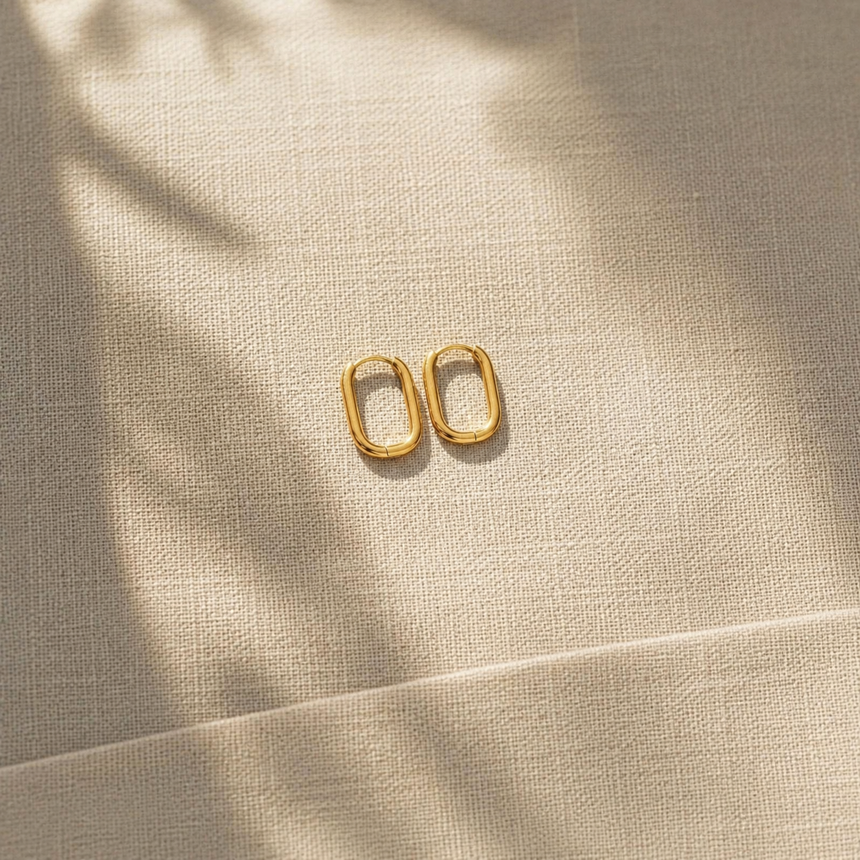 Goldene ovale Creolen auf hellem Leinenstoff mit natürlichem Schatten