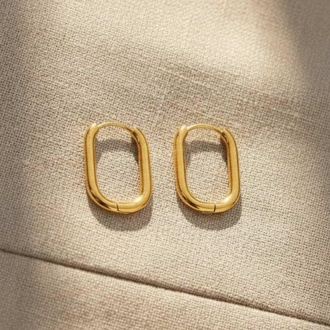 Goldene ovale Creolen als Detailaufnahme auf beigem Stoff