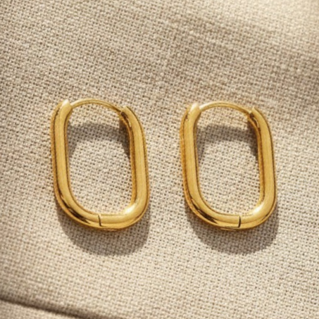 Goldene ovale Creolen als Detailaufnahme auf beigem Stoff