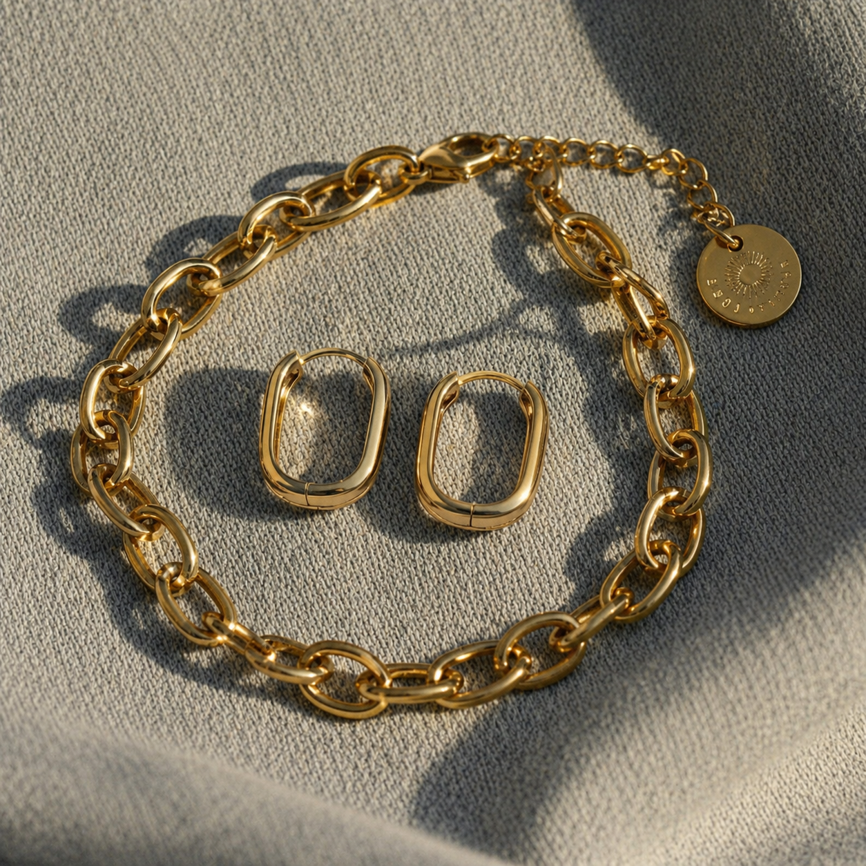 Goldene ovale Creolen kombiniert mit goldener Kette auf hellem Denim
