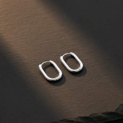 Silberfarbene ovale Creolen aus Edelstahl auf dunklem Untergrund, minimalistisches Design.