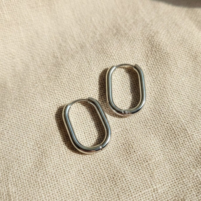 Silberfarbene Ovea Creolen aus Edelstahl 304L in rechteckig-ovaler Form auf beigem Leinen.
