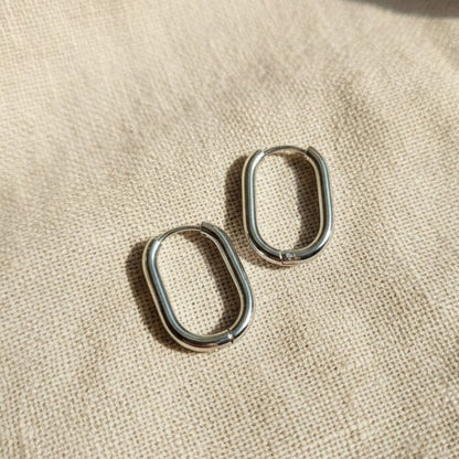 Silberfarbene Ovea Creolen aus Edelstahl 304L in rechteckig-ovaler Form auf beigem Leinen.