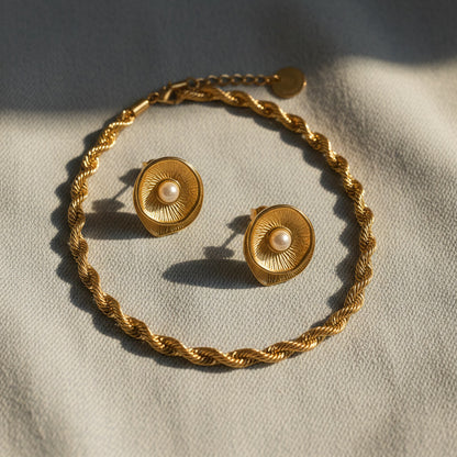 Goldfarbene Perla Vintage-Ohrringe mit Perlendetail neben einer gedrehten Kette auf weichem Stoff.