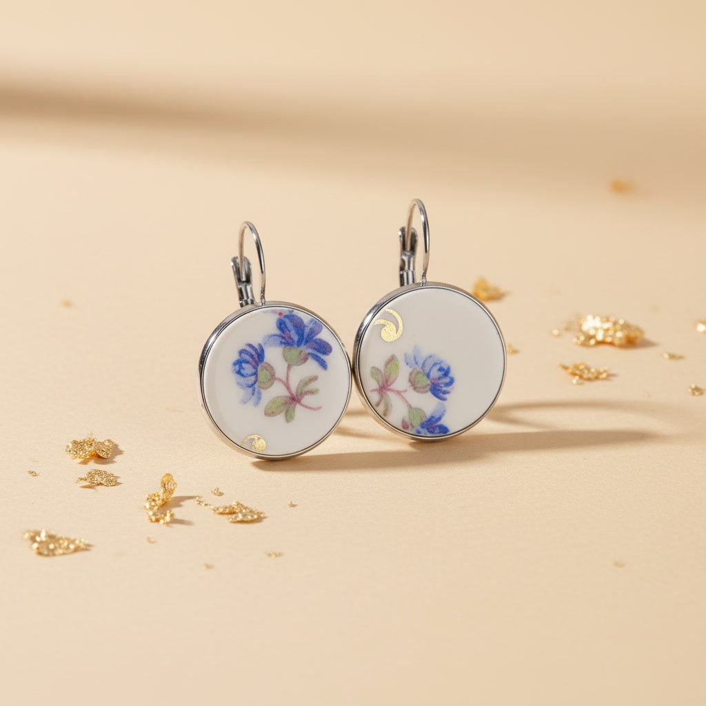 Handgefertigte Porzellanohrringe Modell Caerula von EDELATELIER. Zwei runde Ohrhänger aus weißem Vintage-Porzellan mit einem filigranen, himmelblauen Blüten-Dekor. Die Porzellanelemente sind in silberfarbene Fassungen aus hochwertigem Edelstahl gefasst und hängen an schlichten Ohrhaken. Das Design kombiniert nostalgische Porzellanmalerei mit modernem, minimalistischem Upcycling-Stil.

Bild 2: Detail- und Materiala