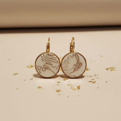 Handgefertigte Porzellanohrringe Ornamenta von EDELATELIER. aus upcyceltem antikem Geschirr mit filigranem grauem Ornament-Muster und goldener Fassung auf beigem Hintergrund mit Goldflocken.
