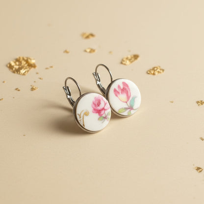 Nahaufnahme der Venusta Ohrringe vor ihrem originalen antiken Porzellanteller. Man erkennt deutlich die Übereinstimmung der handgeschliffenen Fragmente mit dem floralen Dekor des Tellers, was die handgefertigte Qualität und den Upcycling-Gedanken von EDELATELIER. visualisiert. Der Fokus liegt auf der glatten Oberfläche des Porzellans und der präzisen Einfassung, während der Teller im Hintergrund die Geschichte des Schmuckstücks erzählt.