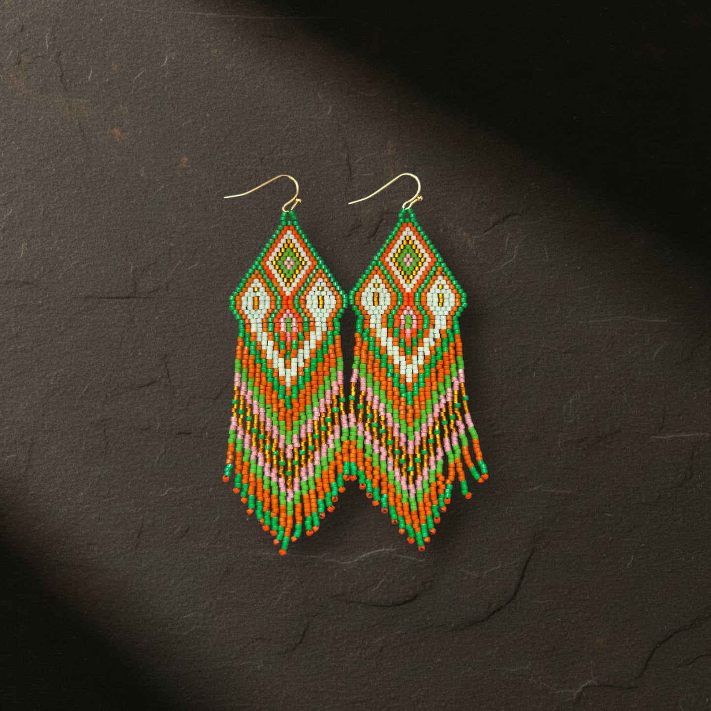 Ein Paar handgewebte Boho-Ohrringe aus Miyuki-Perlen in Grün, Orange, Pink und Weiß von EDELATELIER., frontal fotografiert auf einem dunklen, strukturierten Schieferstein.