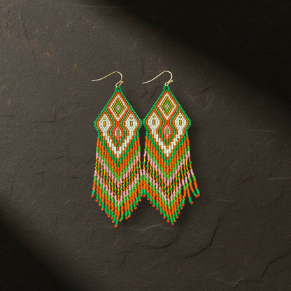 Ein Paar handgewebte Boho-Ohrringe aus Miyuki-Perlen in Grün, Orange, Pink und Weiß von EDELATELIER., frontal fotografiert auf einem dunklen, strukturierten Schieferstein.