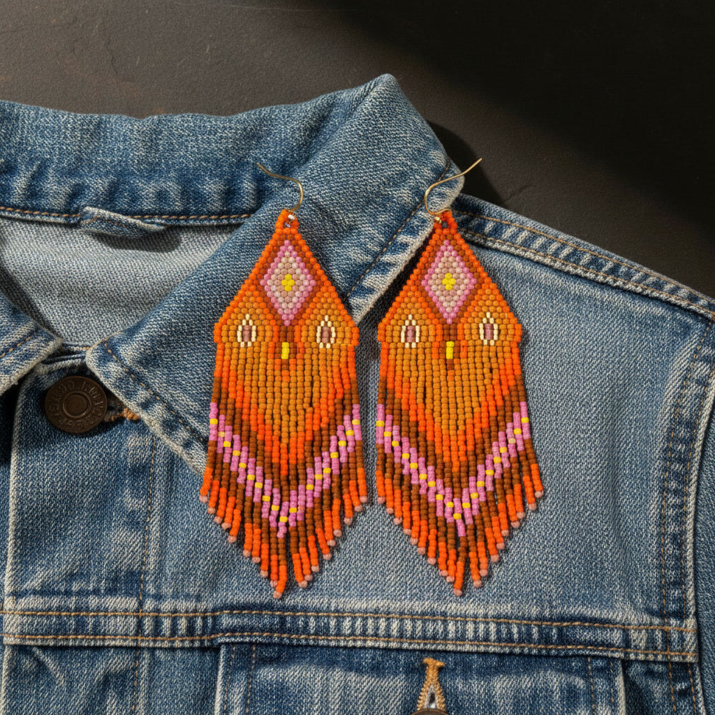Die orange-pinkfarbenen Perlenohrringe liegen auf einer hellblauen Denim-Jeansjacke. Der Kontrast zwischen dem blauen Stoff und den warmen Schmuckfarben unterstreicht den sommerlichen Boho-Stil der handgefertigten Unikate.