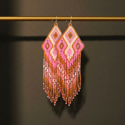 Handgewebte lange Statement-Ohrringe Rosa Antico von EDELATELIER. in mattem Altrosa und Gold mit geometrischem Rautenmuster, frontal fotografiert vor einem dunklen Hintergrund, hängend an einer goldenen Stange.