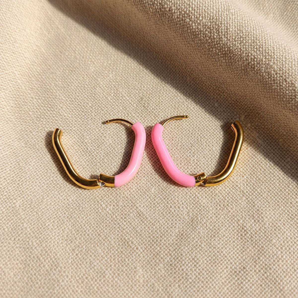 Geöffnete Rosa Creolen Gold Rosa mit sichtbarem Klappverschluss auf beigem Leinen.