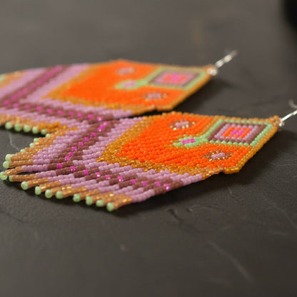 Eine detaillierte Makroaufnahme der "Rosa di Selva" Ohrringe auf einer dunklen Schieferplatte. Die präzise gewebten Miyuki-Glasperlen in Pink, Orange und dunklen Akzenttönen zeigen ein kunstvolles geometrisches Webmuster.