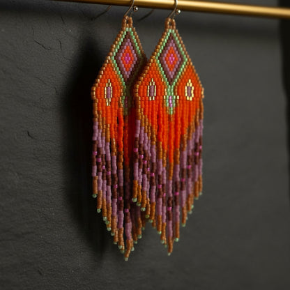 Seitliche Nahaufnahme der handgefertigten Statement-Ohrringe Rosa di Selva von EDELATELIER. Der Fokus liegt auf der filigranen Struktur der Miyuki-Perlen in leuchtendem Orange und Pink, während der weiche Fall der Fransen die Dynamik und Leichtigkeit des Designs unterstreicht.