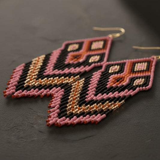 Eine detaillierte Makroaufnahme der "Rosa Notte" Ohrringe auf einer dunklen Schieferplatte. Die präzise gewebten Miyuki-Perlen in tiefem Schwarz und pudrigen Rosétönen zeigen ein kunstvolles geometrisches Webmuster mit feinen Details.