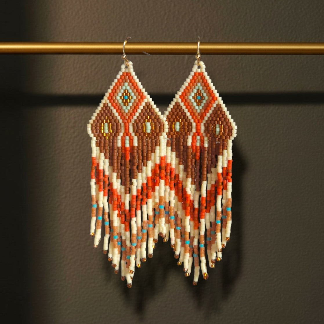 Ein Paar lange Boho-Ohrhänger Sabbia Dorata von EDELATELIER., die elegant an einer goldenen Stange hängen und die feinen Perlenfransen sowie die goldfarbenen Edelstahl-Ohrhaken betonen.