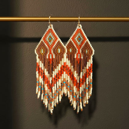 Ein Paar lange Boho-Ohrhänger Sabbia Dorata von EDELATELIER., die elegant an einer goldenen Stange hängen und die feinen Perlenfransen sowie die goldfarbenen Edelstahl-Ohrhaken betonen.