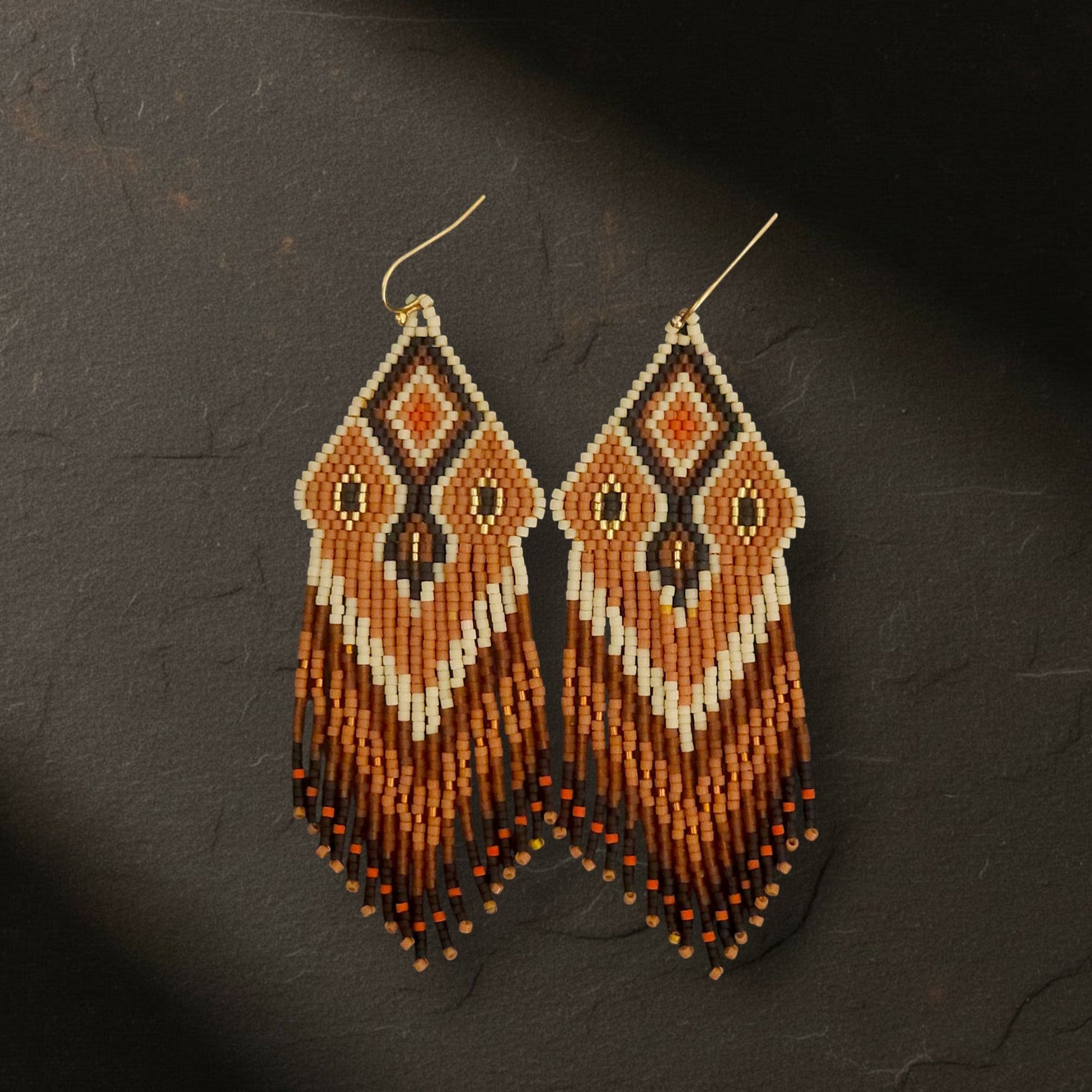 Handgefertigte Statement-Ohrringe mit geometrischem Rautenmuster aus japanischen Miyuki Delica Perlen in Orange, Terracotta, Schwarz und Beige.
Die langen Perlenfransen hängen an goldfarbenen Ohrhaken.
