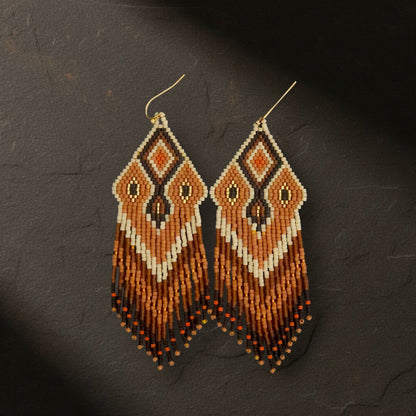 Handgefertigte Statement-Ohrringe mit geometrischem Rautenmuster aus japanischen Miyuki Delica Perlen in Orange, Terracotta, Schwarz und Beige.
Die langen Perlenfransen hängen an goldfarbenen Ohrhaken.