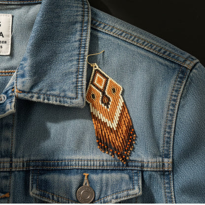Die terrakotta-braunen Perlenohrringe liegen auf einer dunkelblauen Denim-Jeansjacke. Der Kontrast zwischen dem derben Stoff und der filigranen Perlenarbeit unterstreicht den modernen Boho-Stil der Schmuckstücke.