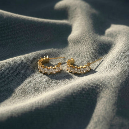 Goldfarbene Scintilla Zirkonia-Creolen auf hellem Denimstoff im Sonnenlicht.