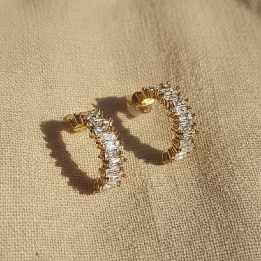 Scintilla Zirkonia Creolen in Gold auf hellem Leinenstoff mit warmem Licht und Schatten.
